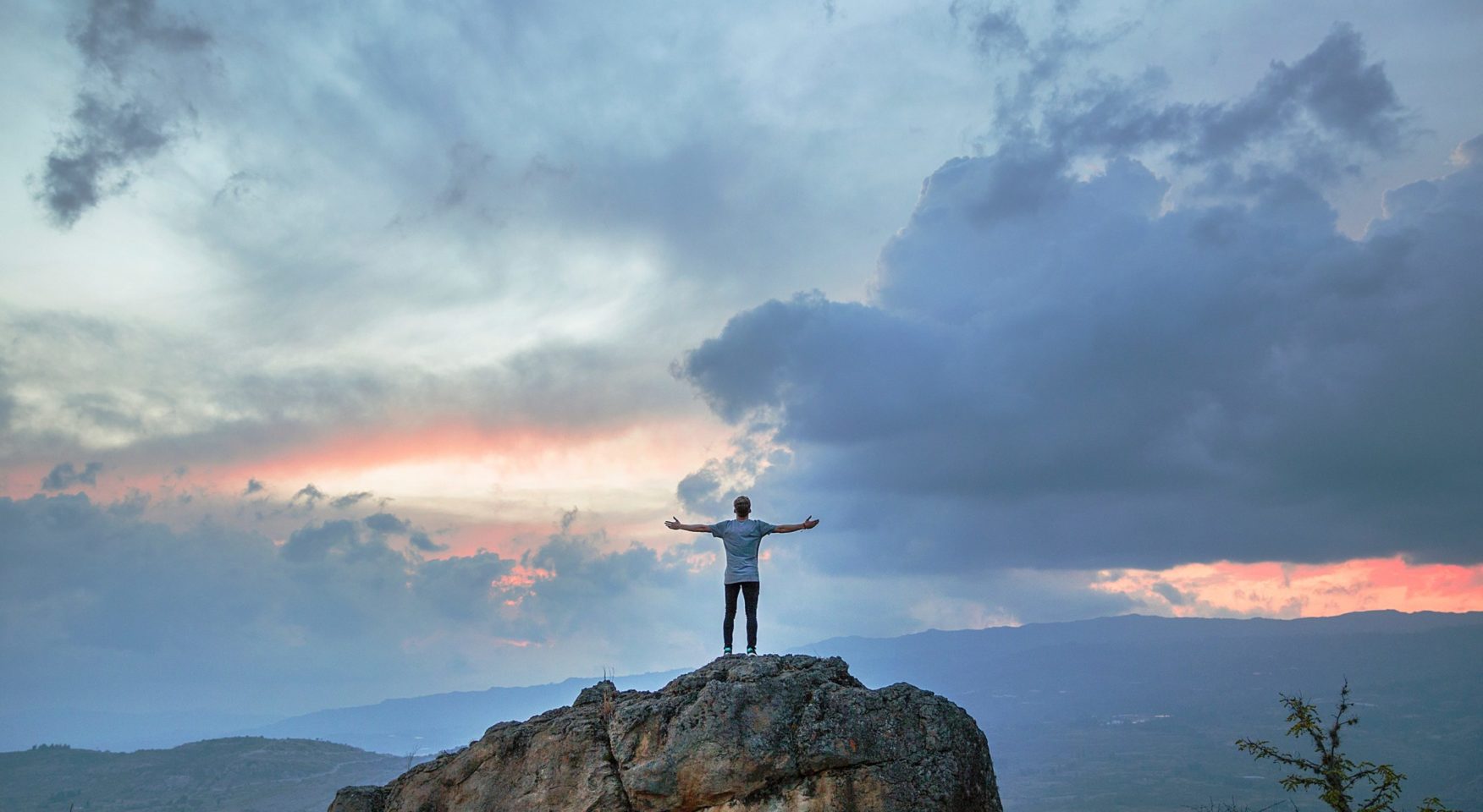 Man standing with his arms open atop rock